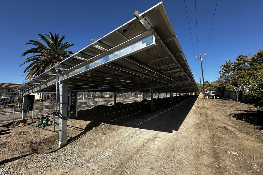 The steel frame of a solar canopy before the modules are set, palms and hills behind