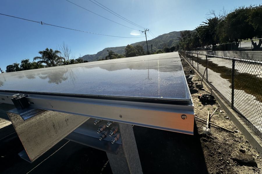 A solar canopy with most of its modules installed, mountains in the distance