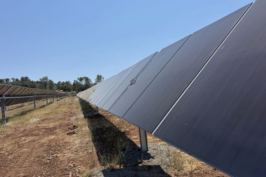 A long row of solar modules on single-axis trackers, dry ground beneath
