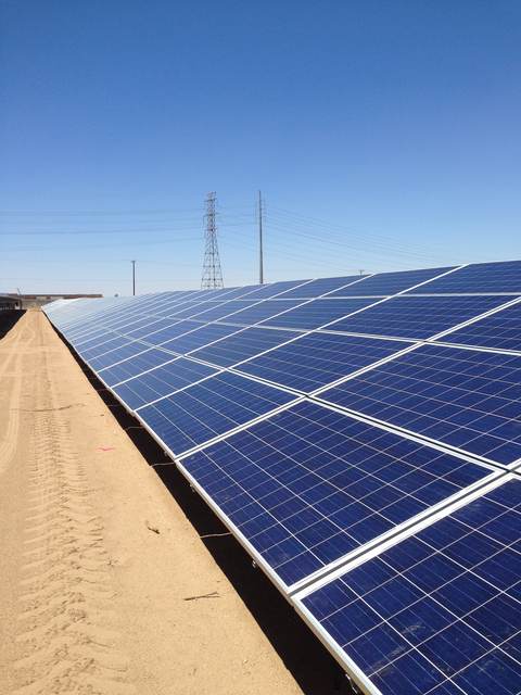 Ground-mount panel row on desert sand under transmission lines