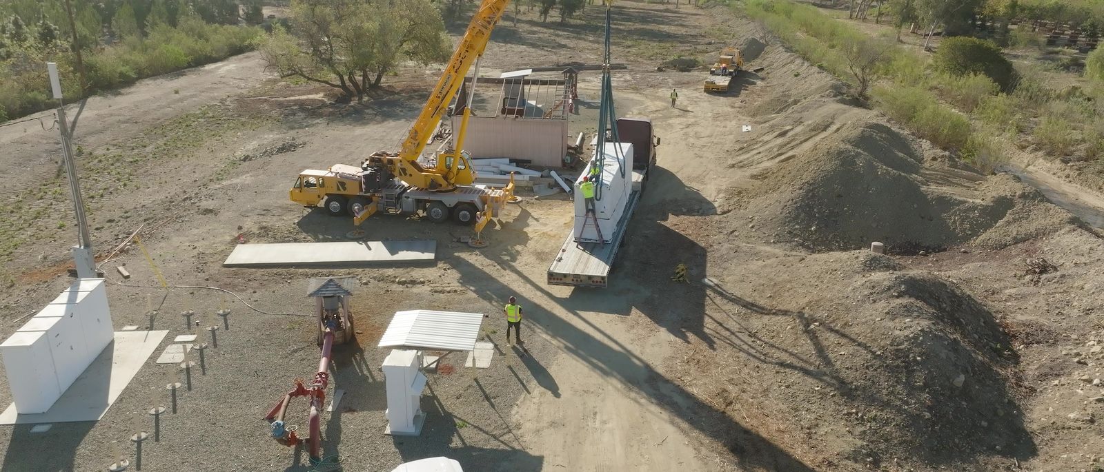 A crane working beside a prepared pad with an enclosure rigged for lifting