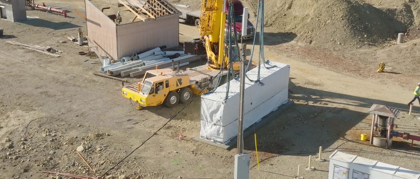 A battery enclosure being lowered by crane onto a concrete pad at a well site